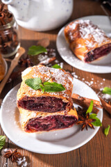 Homemade fragrant autumn cherry strudel with raisins, nuts, honey, cinnamon spices, on plate on kitchen table copy space 