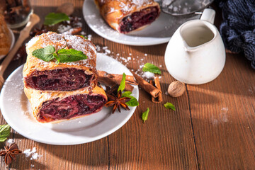 Homemade fragrant autumn cherry strudel with raisins, nuts, honey, cinnamon spices, on plate on kitchen table copy space 