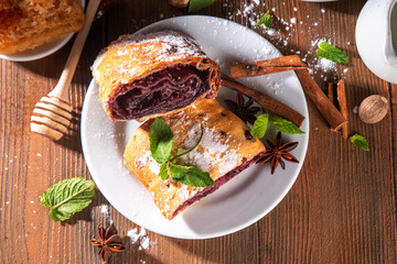Homemade fragrant autumn cherry strudel with raisins, nuts, honey, cinnamon spices, on plate on kitchen table copy space 