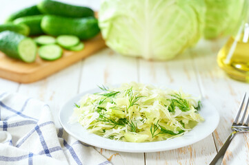 Spring vegan salad with cabbage, cucumber and dill on a white wooden table, selective focus.