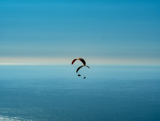two paraglider sails soar through the air against a  blue sky and sea to create a scene of enchantment