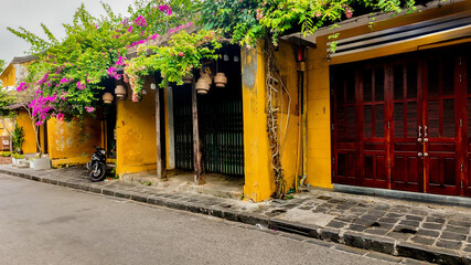Quaint street in Hoi An, Vietnam, showcasing yellow-walled buildings draped in vibrant...