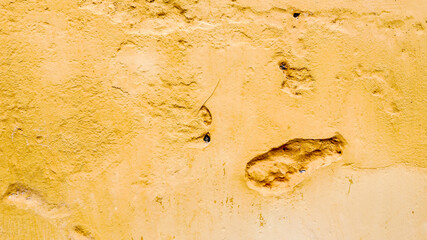 Old peeling yellow plaster wall with cracks and dents, signifying deterioration and home maintenance problems