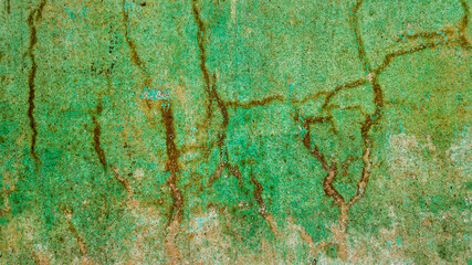 Old green wall surface with peeling paint and cracks depicting urban decay and weathering effects