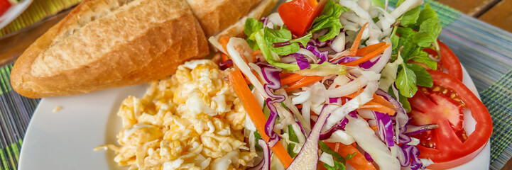 A colorful plate of scrambled eggs, fresh vegetable salad, and crusty bread, perfect for a healthy breakfast or brunch