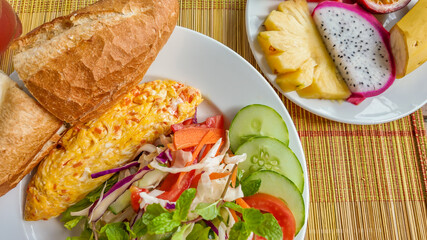 A vibrant, healthy breakfast plate featuring an omelette, fresh salad, baguette, and exotic fruits, ideal for New Year health resolutions
