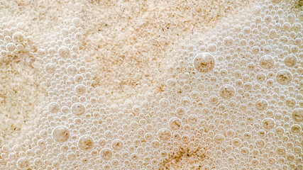 Close-up of foam bubbles on wet beach sand, capturing the essence of summer relaxation and coastal environmental concepts