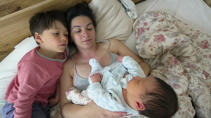 Family moment - mother and son admire newborn baby resting in bed, welcoming the newest family...