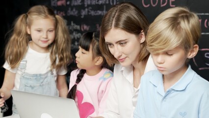 Young smart teacher using laptop to teach diverse student programing system. Caucasian learner looking at computer screen while study about coding prompt at blackboard with program code. Erudition.