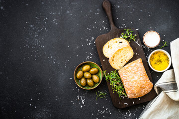 Ciabatta bread with olives and herbs on black. Mediterranean food. Top view with copy space.