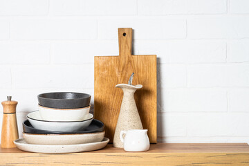 Kitchen table, kitchen utensils, plates, bowls, shakers and wooden cutting board, white modern interior. Modern kitchen interior.