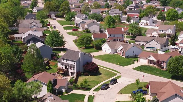 Tranquil american suburb from a bird's eye view. Neat rows of homes, lush lawns, and treelined streets under a clear blue sky. Serene community living