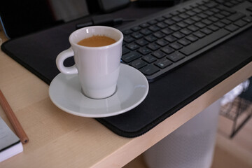 A white cup of espresso and a man typing on a keyboard	