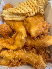 Fried, battered fish and chicken planks with waffle fries in a basket