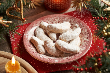 Homemade Christmas cookies called Kipferl or vanilla crescents coated in sugar on a vintage plate with decorated spruce tree branches