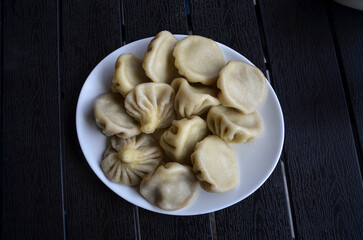 Delicious georgian dumplings khinkali pinched at the top flavorful meat filling inside served on a white plate, on a dark wooden surface. Perfect for food blogs, recipe websites, and culinary content