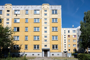 Older high-rise apartment block for social housing with yellow cladding against a blue sky, large...