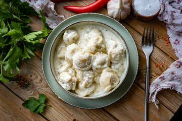 Dumplings with meat filling in cream sauce in a plate on a wooden table. Ravioli with meat for lunch. Close-up