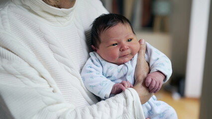 Close-up newborn baby held in arms by grandmother during first days of life, initial stages of...
