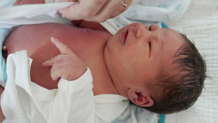 Newborn Baby - Mother Dressing Infant's Hands, Close-Up. A tender moment showing a mother dressing her newborn son's tiny hands, highlighting the nurturing bond between mother and child