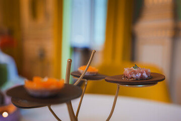 Sophisticated interior of a luxury hotel dining area featuring a multi-tiered serving stand with elegantly plated appetizers. Opulent decor with golden accents and plush yellow seating.