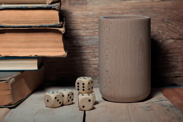 drewniane kości do gry i kubek do kości jako symbol hazardu na tle książek w bibliotece © Henryk Niestrój