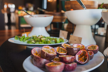 Close-up of a plate with halved passion fruits and sliced kiwi at a luxurious buffet. Elegant white bowls and warm lighting enhance the sophisticated decor.