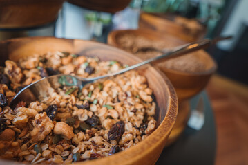 A detailed view of a wooden bowl filled with granola, nuts, seeds, and dried fruits, set in a luxury hotel dining area. Elegant presentation with rustic charm.