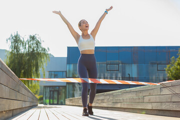 Athletic fitness sport runner girl finishing racing competition. Victory and success. Workout cardio training in city park. Young woman jogger champion winning marathon. Active sportswoman motivation.