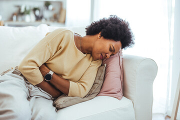 Shot of a young woman experiencing stomach pain while lying on the sofa at home. Attractive young woman lying down on her bed and suffering from period pains at home