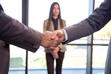 Two men shake hands in front of a woman