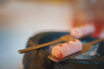 A detailed view of two sushi-like rolls garnished with orange dots and green herbs, placed on metal...