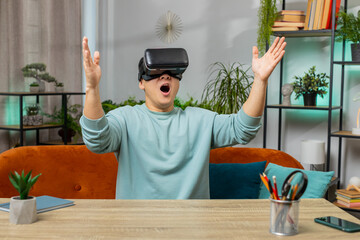 Asian man using virtual reality futuristic technology VR app headset helmet typing on virtual keyboard, play simulation 3D 360 online video game at home apartment. Guy in goggles sitting on sofa