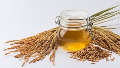 Rice bran oil in a glass jar with rice paddy grains beside it, isolated on white background. Showcasing the natural beauty and health benefits of this versatile ingredient