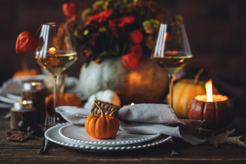 Beautiful elegant table setting for candlelight Thanksgiving Day dinner or Halloween party at home. Fancy dishware, porcelain plates. Floral centrepiece, pumpkins and burning candles as decor