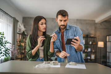 Couple learn from mobile phone how to make a clay figurine, pottery