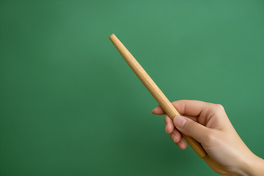 A human hand holds a school pointer on a green background. The beginning of the school year. A teacher points to the blackboard. Education.