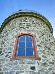 Fieldstone mill with metal roof. Mill tower under a blue sky. Brick tower with old wooden frame window. 