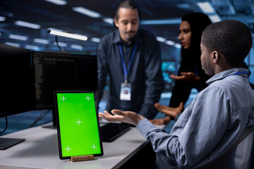 Focus on green screen tablet used by team in blurry background reconfiguring server farm to optimize it for data processing. Close up of mockup device used by workers overseeing data center equipment