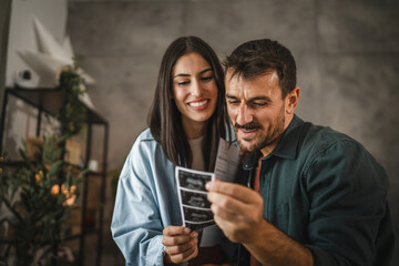 Adult couple stand and hold ultrasound picture of baby from envelope