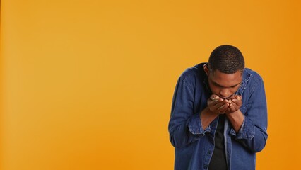 Coffee enthusiast looks at aromatic roasted beans against orange background, promoting cold brew at a coffee shop or cafeteria. Enjoying eco friendly delicious black seeds. Camera B.