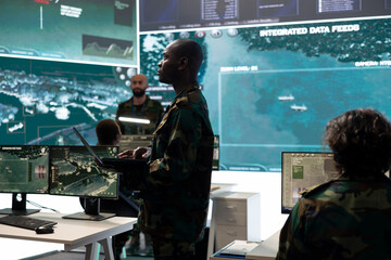 Intelligence analyst comparing satellite surveillance data before transmitting battlefield...