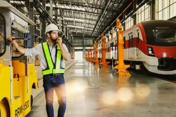 Male worker wearing safety suit during work driving yellow locomotive for towing  standing reporting with walkie talkie in building electric train station electric tram transportation system.