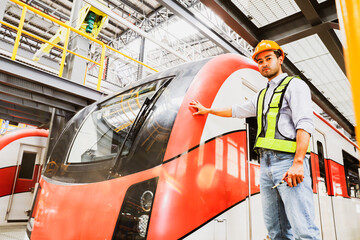 Asian male handsome operator operator engineer standing in front of electric locomotive at modern electric train maintenance station checking safety systems before using city transportation service.
