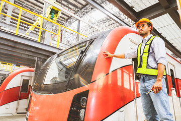 Asian male handsome operator operator engineer standing in front of electric locomotive at modern electric train maintenance station checking safety systems before using city transportation service.