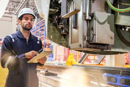 Male worker engineer standing in front locomotive diligently holding laptop in front electric locomotive at modern maintenance station, preventive quality inspection system, safety rail equipment.