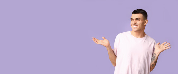 Handsome ashamed young man shrugging on lilac background