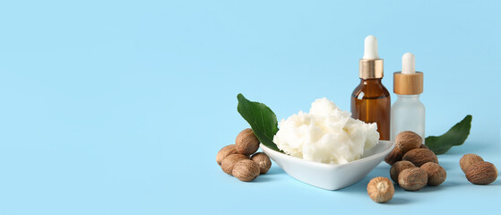 Bowl of shea butter with bottles of cosmetic oil and nuts on blue background