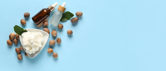 Bowl of shea butter with bottles of cosmetic oil and nuts on blue background