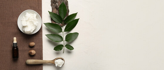 Bowl of shea butter with bottle of cosmetic oil and nuts on white background
